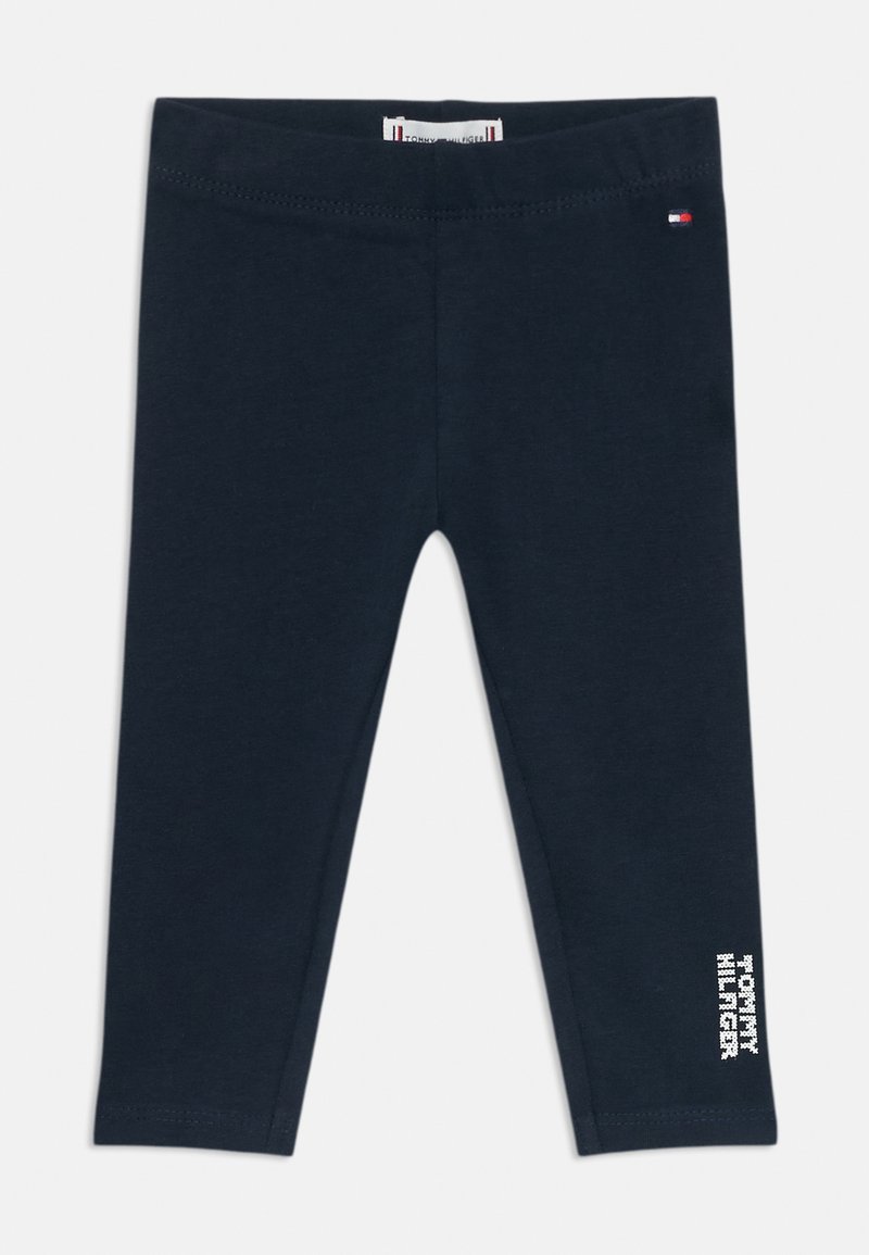 Legginguri bleumarin din material moale din bumbac, cu un tiv cusut la talie și un grafic de text alb pe piciorul stâng. Fără modele sau accesorii.