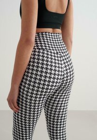 Legginsy z wysokim stanem w czarno-biały wzór pepitki, wykonane z elastycznego materiału, o gładkiej, dopasowanej sylwetce.