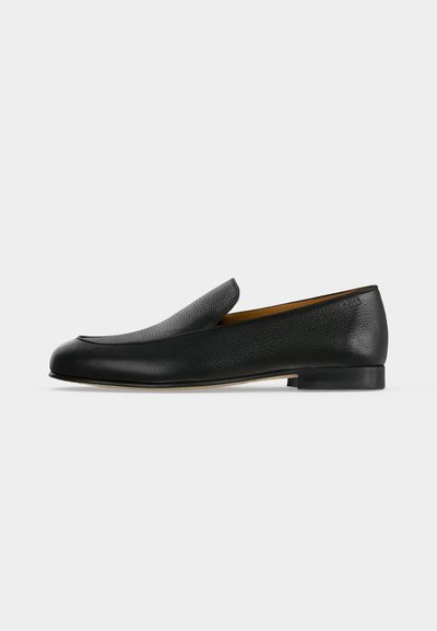 Mocassin noir en cuir à enfiler, avec un petit talon et un bout arrondi, présenté de profil sur un fond clair uni.