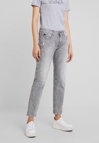 Jeans de mezclilla gris con una textura ligeramente desgastada, diseño de pierna recta, cinco bolsillos y una apariencia sutilmente desvaída. Combinados con zapatillas blancas.