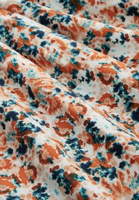 Tessuto con motivo floreale astratto in arancione, teal e blu navy su sfondo bianco, con una texture morbida e liscia e pieghe drappeggiate.