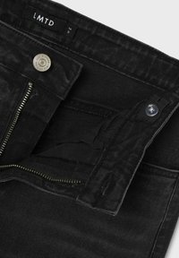 Czarne dżinsy z zamkiem błyskawicznym z przodu, zapięciem na srebrny guzik oraz metką z napisem "LMTD." Tkanina ma teksturowany wzór.