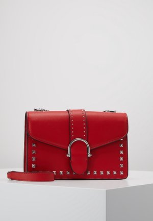 Red leather crossbody bag with silver studs and a rounded silver clasp, displayed on a white pedestal against a plain background.