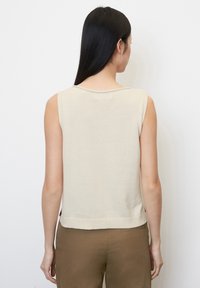Top senza maniche di un beige chiaro con scollo rotondo e una vestibilità leggermente ampia, realizzato in un morbido materiale a maglia. Design semplice senza motivi.