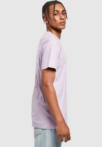 T-shirt en coton violet clair avec des manches courtes et un col rond, porté par une personne avec un jean bleu clair. Design simple et dépouillé.
