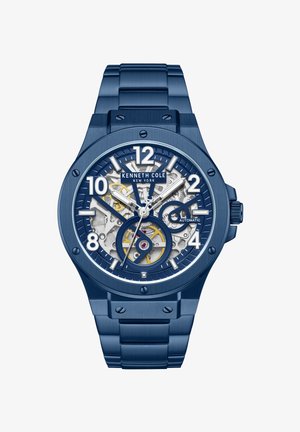 Sininen ruostumattomasta teräksestä valmistettu Kenneth Cole -automaattikello, jonka skeletton-kellotaulu paljastaa kellon sisäiset rattaat ja jossa on valkoiset tuntimerkinnät ja osoittimet.