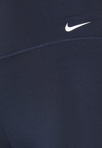 Granatowe legginsy sportowe wykonane z elastycznego materiału o gładkiej fakturze, z białym logo Nike na boku.