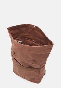 Bruine canvas rugzak met een oprolopening, een voorzak met rits en platte schouderbanden. Gelaagd stof met een minimalistisch ontwerp.