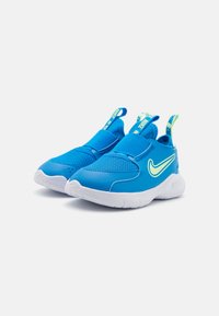 Des chaussures de sport bleues avec une tige en mesh et synthétique. Elles présentent une semelle blanche, des courroies élastiques sur les côtés et un accent vert néon sur le logo.