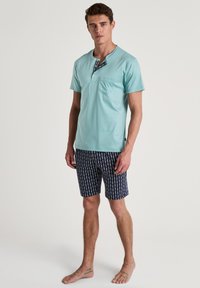 Lichtblauw overhemd met korte mouwen en een zak, met een gemusterde halslijn. Gecombineerd met donkerblauwe shorts met een subtiel herhaald patroon.