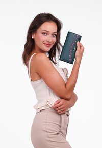 Green leather wallet with a curved maroon accent featuring circular cutouts. Compact design, smooth texture, and subtle branding detail.