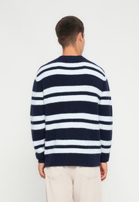 Maglione a righe blu navy e azzurro chiaro lavorato a maglia con texture a coste e scollo tondo, dotato di maniche lunghe e una vestibilità comoda.