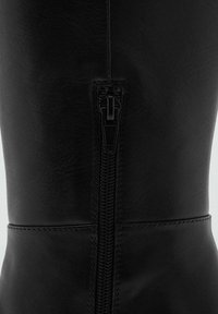 Bota de cuero negro hasta la rodilla con cremallera lateral, textura suave y detalles de costura a lo largo de las costuras.