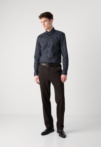 Marineblå skjorte med hvite prikker, kombinert med svarte dressbukser og svarte sko. Skjorten har krage og lange ermer.