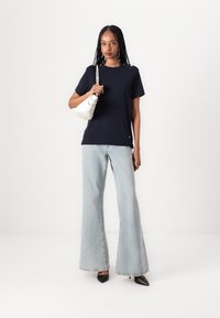 Marinblå t-skjorte med korte ermer parret med lyseblå vide jeans. Tilbehør med en liten hvit håndveske og svarte spisse hæler.