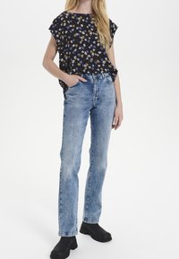 Černá blůza s květinovým potiskem a krátkými rukávy, v kombinaci se světle modrými džíny rovného střihu a černými kotníkovými botami.
