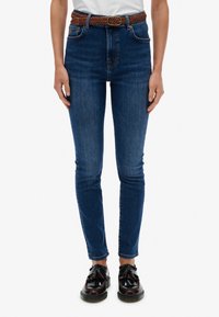 Vaqueros de tiro alto en azul con ajuste slim, hechos de denim. Cuenta con un cinturón trenzado marrón y dos bolsillos frontales, con un ligero desgaste.