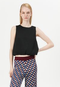 Zwarte mouwloze crop top met een ronde halslijn, gecombineerd met patroonachtige wijde broek met geometrische vormen in rood, blauw en crème.