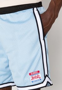 Blå meshshorts med svart kant, med ett röd och blått märkespatch på vänster ben. Tyget har en andningsbar, perforerad struktur.