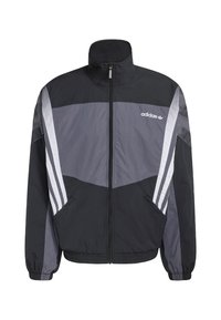 Čierna a sivá vetrovka s vysokým golierom, predným zipsom, bočnými vreckami a bielymi pruhovanými detailmi na rukávoch. Na hrudi je logo Adidas.
