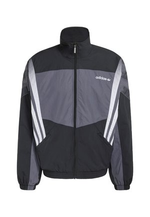 Čierna a sivá vetrovka s vysokým golierom, predným zipsom, bočnými vreckami a bielymi pruhovanými detailmi na rukávoch. Na hrudi je logo Adidas.