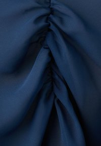 Tessuto blu scuro raccolto saldamente al centro, creando pieghe morbide e piegature strutturate.