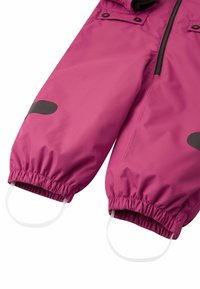 Růžový voděodolný snowsuit se spodními nohavicemi, černými akcentními panely, elastickými manžetami a integrovanými popruhy na nohy. Hladká textura s detaily zipu.