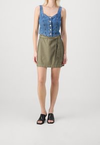 Džínový crop top se zapínáním na knoflíky, doplněný khaki zavinovací sukní. Černé otevřené mule boty dokončují outfit. Jednoduchý a neformální design.