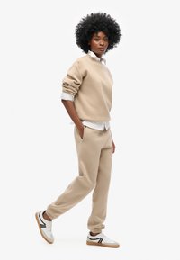 Sudadera de algodón beige con mangas enrolladas, combinada con joggers a juego y zapatillas blancas con rayas negras y suela de goma.