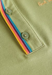 Grøn polo shirt med en tekstureret stof, med en flerfarvet stripe og knaplukning. Broderet mærkenavn i orange.