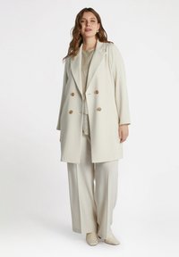 Light beige double-breasted coat with large tan buttons, featuring a tailored design. Paired with beige wide-leg trousers and matching shoes.