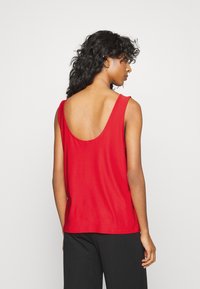 Top vermelho sem mangas com um grande decote nas costas, feito de um tecido suave, apresenta um corte descontraído e textura lisa, ideal para uso casual.