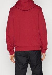 Červená mikina s kapucí a klokaní kapsou, nastavitelné stahovací šňůrky, žebrované manžety a lem. Vyrobena z měkké texturované látky.