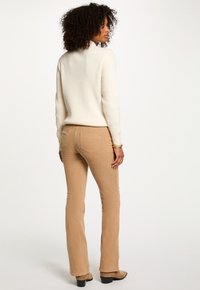 Pantaloni a zampa d'elefante in corduroy beige abbinati a un maglione bianco a costine, che presenta una finitura testurizzata e un design aderente con tasche posteriori.