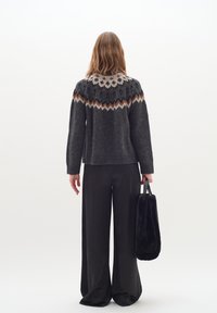 Pulover tricotat de culoare gri închis, cu un guler decorat cu modele florale albe și zigzaguri portocalii. Pantaloni negri, largi, ținând o geantă din blană neagră.