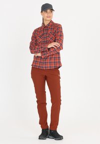 Punainen ja sininen ruudullinen pitkähihaisessa paidassa on napit, ja se on yhdistetty istuviin ruskeisiin housuihin. Mustat kengät viimeistelevät asun.