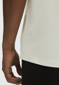 Lichtgekleurde, gestructureerde sportshirt met een lage zoom en logodetail aan de zijkant, gecombineerd met donkere shorts.