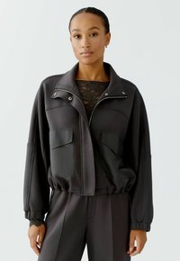Schwarze Bomberjacke mit hochstehendem Kragen, Reißverschluss und zwei vorderen Taschen. Aus glattem Stoff mit lässigem Schnitt und elastischen Bündchen.