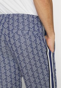 Blå mönstrade joggingbyxor med en texturerad geometrisk design, sidostråk i vitt och marinblått samt en bakfickadetalj.