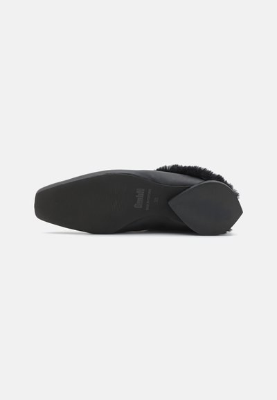 Semelle de chaussure noire avec une surface texturée, une forme légèrement courbée et un design de talon distinct. Accents en fourrure douce le long du bord supérieur.