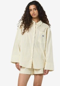 Ribad kollane särg pikkade varukatega, nupuga ees ja rinnataskuga; koos sobivate ribadega lühikeste pükstega; puuvillane kangas.