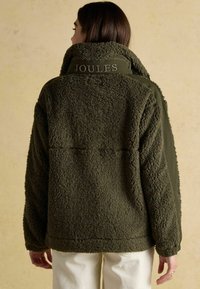 Kurtka polarowa w kolorze oliwkowej zieleni z wysokim kołnierzem, o fakturowanej powierzchni, z haftowanym logo "Joules" na plecach, gładkie kontrastowe rękawy.