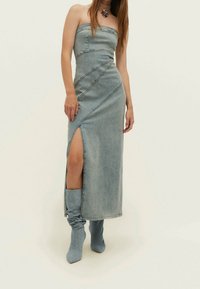 Denim-maksimekko ilman olkahihnoja, jossa on korkea halkio, viistot saumat ja vaaleansininen väri. Yhdistetty yhteensopiviin denim-polvikorkeisiin saappaisiin.