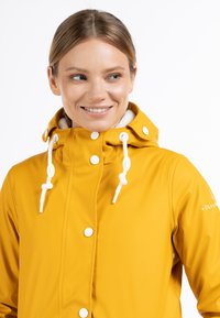 Căciulă de ploaie galbenă, impermeabilă, cu nasturi albi și sireturi, având o căptușeală interioară moale și un glugă. Design curat și elegant.