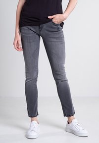 Wąskie szare dżinsy z wypłowiałym wykończeniem, kieszeniami z przodu i prostym dołem, w połączeniu z białymi trampkami.