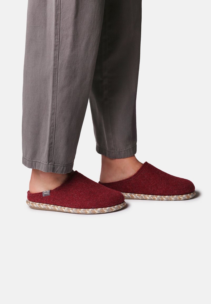Zapatillas de fieltro rojas sin cordones con suela de yute trenzado, que presentan una punta redondeada y un diseño minimalista, combinadas con pantalones grises recortados.