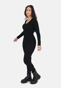 Zwarte jumpsuit met lange mouwen en een ronde halslijn, met een geribde textuur. Gepaard met stevige zwarte legerlaarzen.