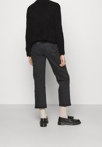 Maglione cropped nero con texture, jeans in denim scuro a vita alta e scarpe nere con pon-pon. Design semplice, taglio dritto e cuciture visibili.