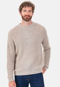 Hellbeiger Strickpullover mit einer strukturierten, gerippten Musterung, rundem Ausschnitt und langen Ärmeln, kombiniert mit dunkelblauen Jeans.