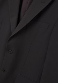 Blazer nero su misura con una texture liscia, due bottoni e una tasca sul petto. Presenta rever affilati e linee pulite.